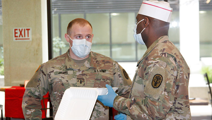 Image of Military health personnel wearing face mask discussing food options. Click to open a larger version of the image.