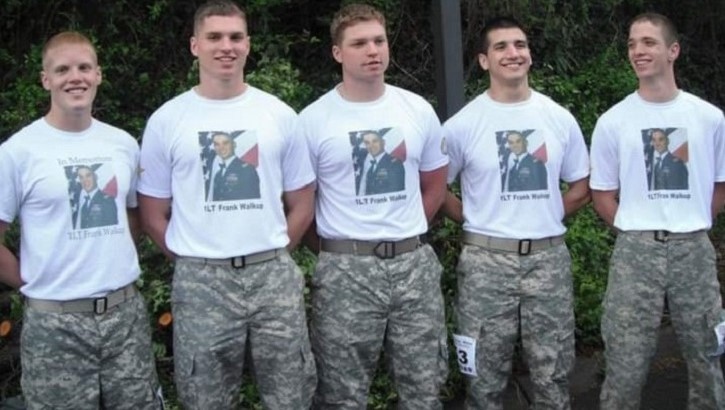 Five young men standing in a line, wearing the same t-shirt and pants