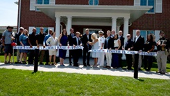 A group of people take part in a ribbon-cutting ceremony in front of the 100th Fisher House