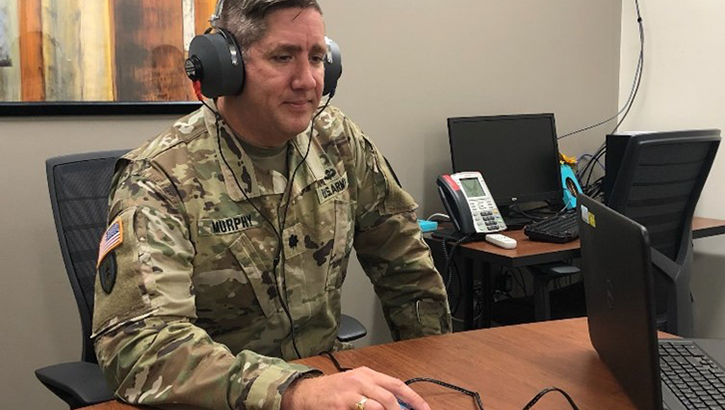 A service member wears headphones while sitting at a desk.