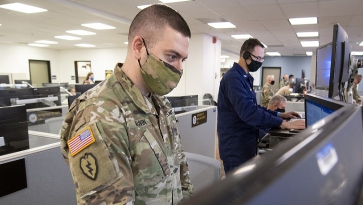 Soldier wearing mask, standing at computer monitors in an office building
