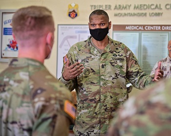 Military personnel wearing a face mask speaking to a group of military personnel