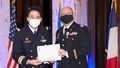 Two military officers on stage; one handing the other a certificate