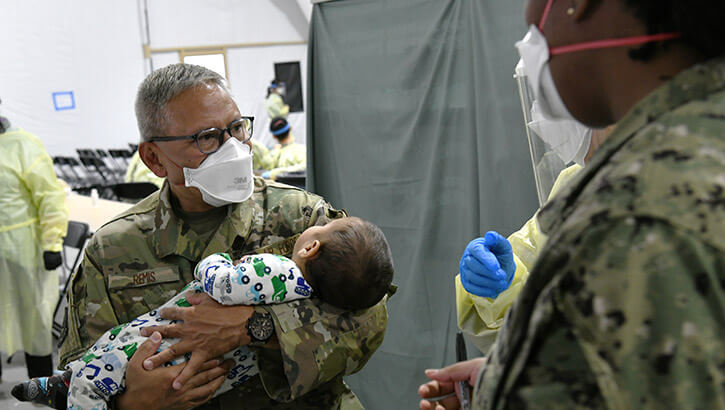 Washington Air National Guard Master Sgt. Andy Remis, assigned to the 116th Air Support Operations Squadron, Camp Murray, Wash., lends a helping hand, holding an Afghan child at the Task Force Liberty Village medical station, Joint Base McGuire-Dix-Lakehurst, New Jersey, Sept. 11, 2021.