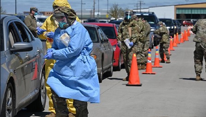 Image of Military personnel performing nasal swabs of people in a row of cars. Click to open a larger version of the image.