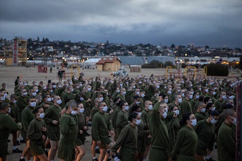 A large group of military personnel wearing face masks, listening to someone speak