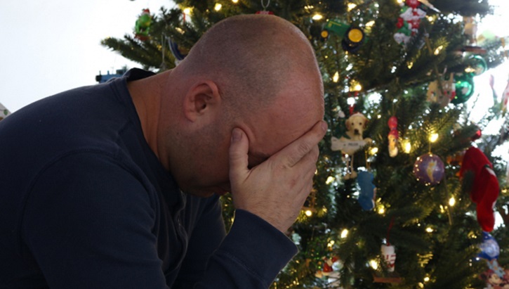 Man with his head in his hands, sitting in front of a Christmas tree