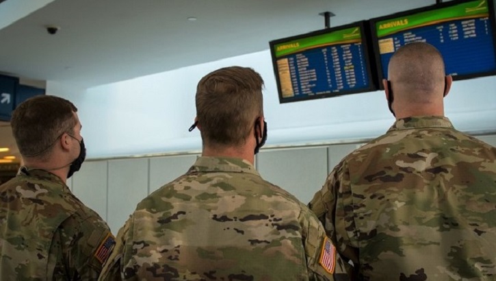 Image of Soldiers wearing masks, looking at flight information in airport. Click to open a larger version of the image.
