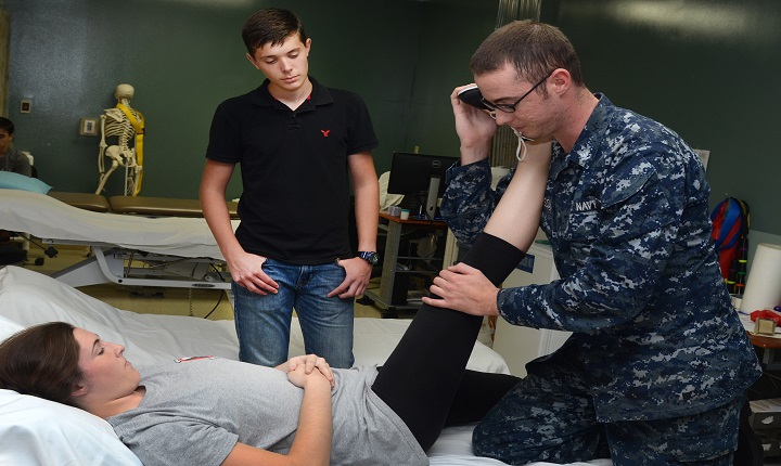 Matthew Alderman (center), a Darnell-Cookman School of the Medical Arts student, observes Navy Hospital Corpsman 3rd Class Daniel Anderson (right), of Naval Hospital Jacksonville’s physical therapy department, performing lower-back therapy on Allyson VanHook. Alderman is participating in the hospital’s annual Science, Service, Medicine and Mentoring (S2M2) program. The program allows selected students to receive real-world experiences in patient care areas—from the operating room and emergency department to pharmacy and physical and occupational therapy.  (U.S. Navy file photo by Jacob Sippel).