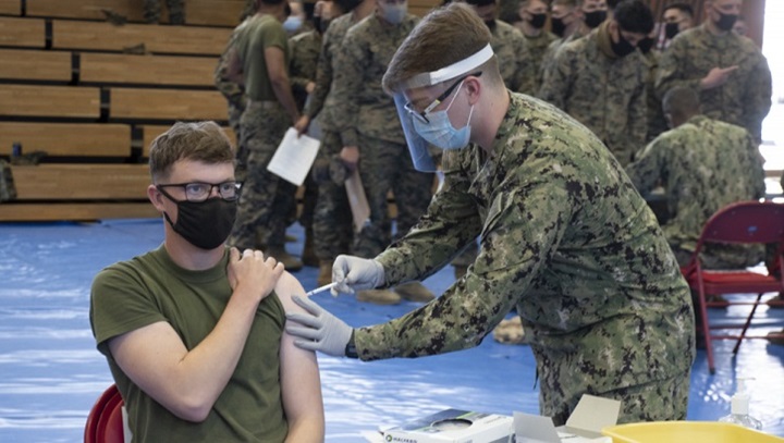 Image of Military personnel wearing a face mask and a face shield administering the COVID-19 vaccine.