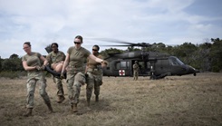 Exercise participants offload a simulated patient from an HH60M Black Hawk helicopter during a Joint Critical Care Field Training Exercise