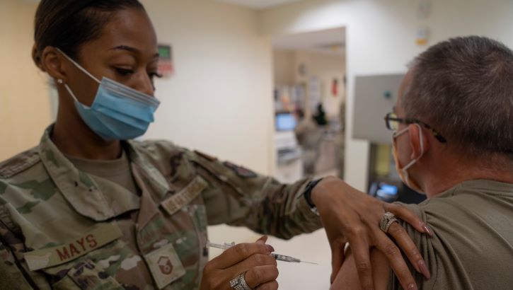 Image of Military health personnel wearing a face mask administering the COVID-19 vaccine. Click to open a larger version of the image.