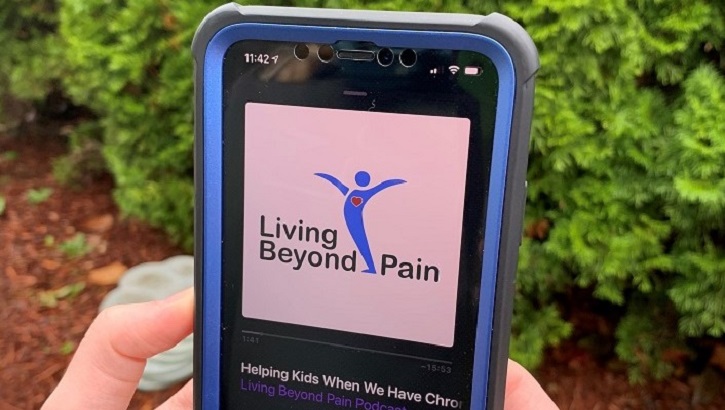 Hands holding a smartphone with the Living Beyond Pain podcast playing on the device.