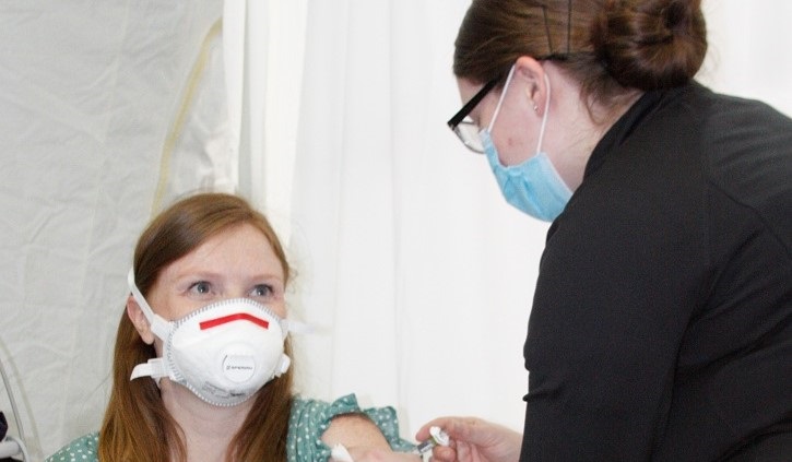 Image of Nurse giving a shot to a girl; both wearing masks. Click to open a larger version of the image.