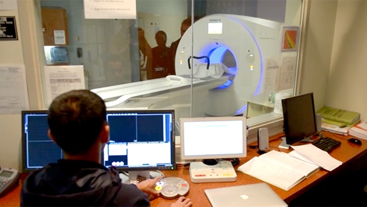 Image of  U.S Navy MRI technologist behind a computer screen with a magnetic resonance machine in the background.