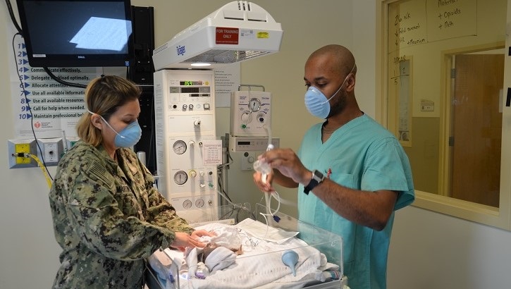 Two medical personnel with a simulated baby in a medical setting