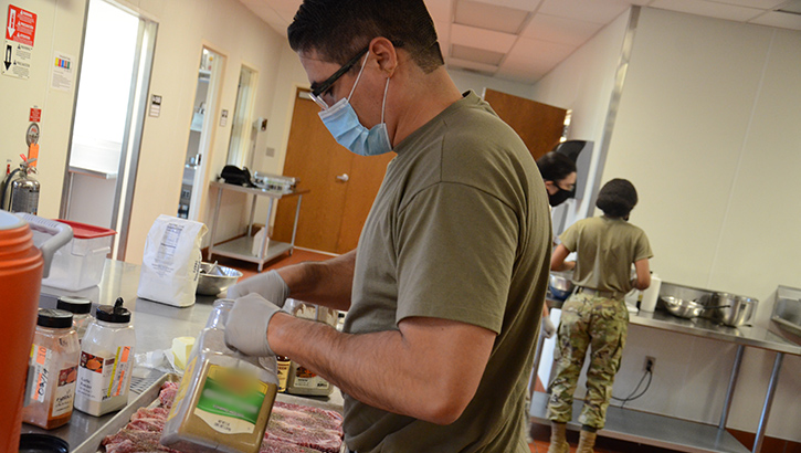 Military health personnel preparing food trays while wearing a face mask