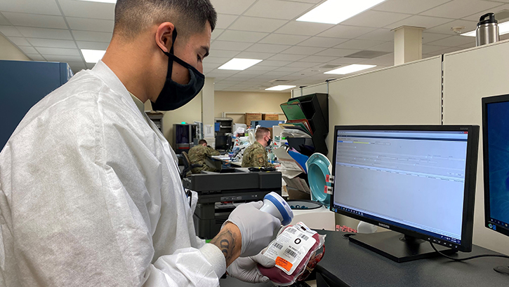 Image of Technician wearing a mask, scanning in a label on a unit of blood.