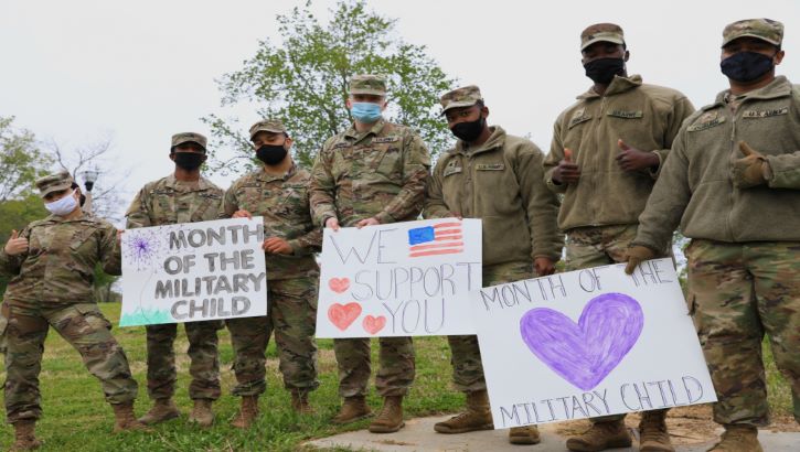 Image of Military personnel wearing face mask holding up posters for Month of the Military Child. Click to open a larger version of the image.