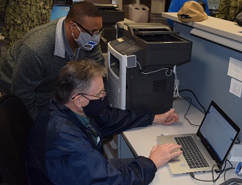 Military personnel wearing face mask working on a laptop computer