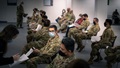 Military personnel wearing face mask sitting in a line waiting for their COVID-19 vaccine