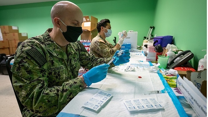 Image of Military personnel wearing face mask getting people ready for the COVID-19 vaccine. Click to open a larger version of the image.