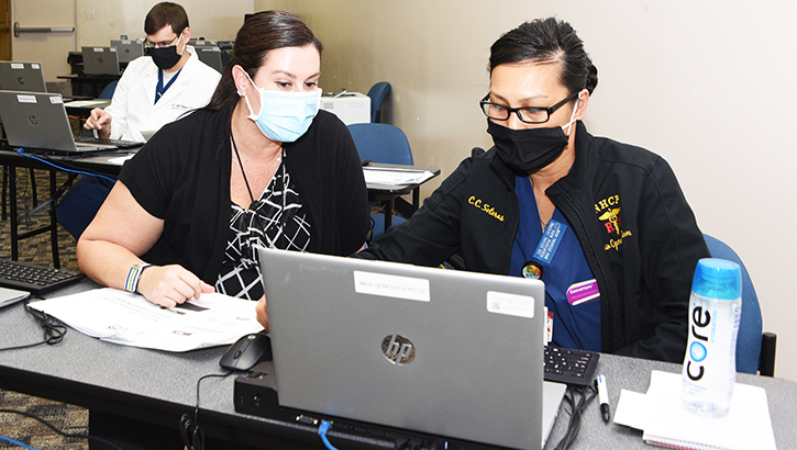Two women in masks, sitting at laptop