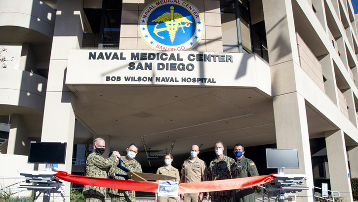 Military personnel wearing face mask standing in front of the Naval Medical Center in San Diego cutting a red ribbon