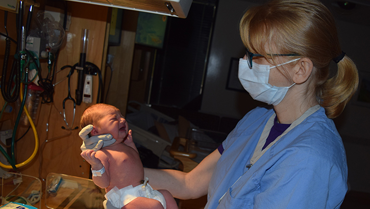 Image of Military health personnel wearing a face mask examining a new born baby.