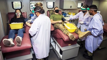 Two people laying on tables, donating blood, surrounded by medical personnel