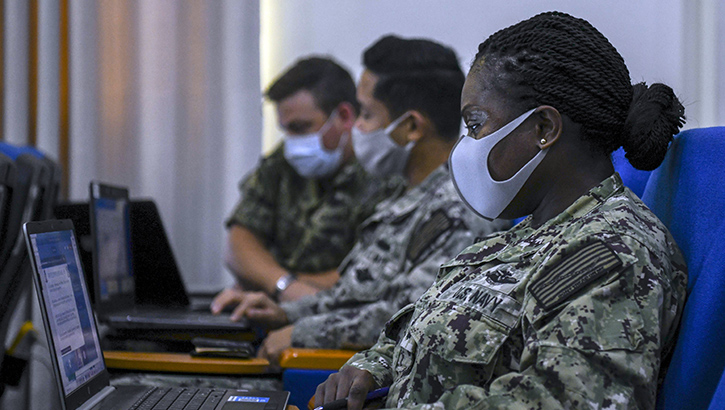 Picture of military personnel wearing a face mask looking at a laptop computer