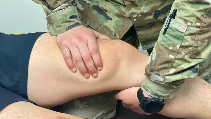 A soldier performs a physical examination of a patient's knee.