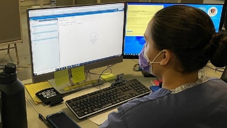 Image of soldier, wearing a mask, in front of a computer screen