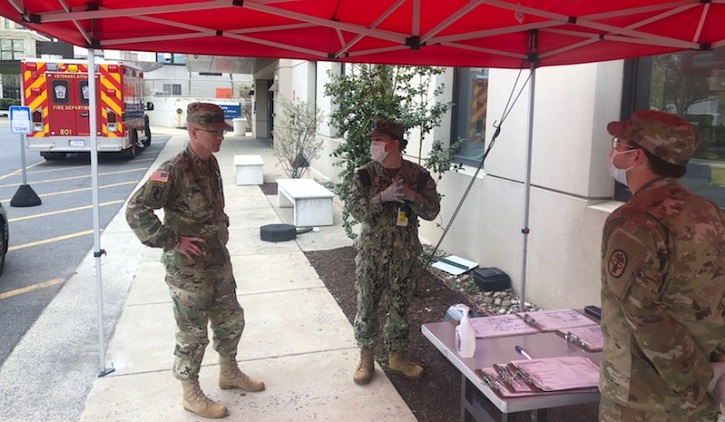 Army Lt. Gen. Ron Place and two soldiers stand at a table with COVID-19 testing supplies
