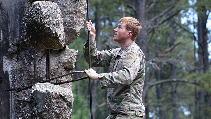 A student assigned to the U.S. Army John F. Kennedy Special Warfare Center and School climbs up an obstacle