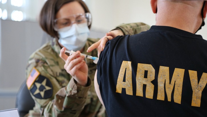 Image of Military health personnel wearing a face mask giving someone the COVID-19 Vaccine. Click to open a larger version of the image.