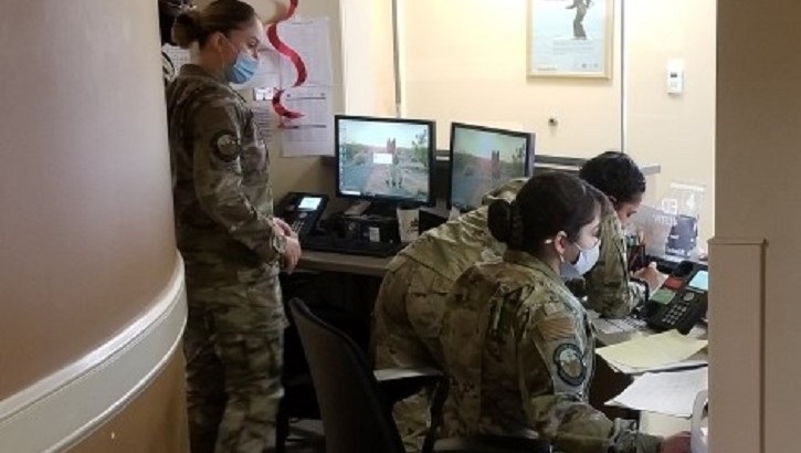 Image of Military personnel standing and sitting at a desk with multiple computer screens.