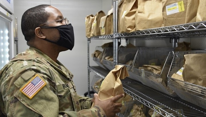 Image of Military pharmacist, wearing a mask, looking at bags of prescriptions.