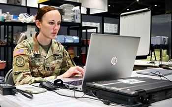 Military personnel typing on a laptop in an office