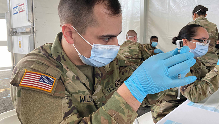 Image of Military personnel wearing a face mask filling up syringes with the COVID-19 vaccine. Click to open a larger version of the image.