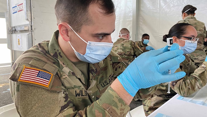 Image of Military personnel wearing a face mask filling up syringes with the COVID-19 vaccine.