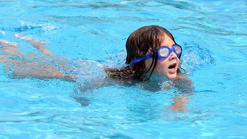 Little girl in goggles swimming in pool