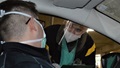 Two men wearing masks, one in a car, one leaning in the car