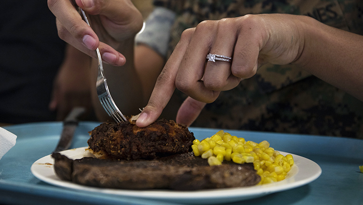 Woman cutting a steak on a plate, with corn