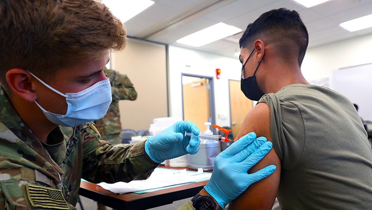 Image of An Army medic administers the COVID-19 vaccine to another soldier.