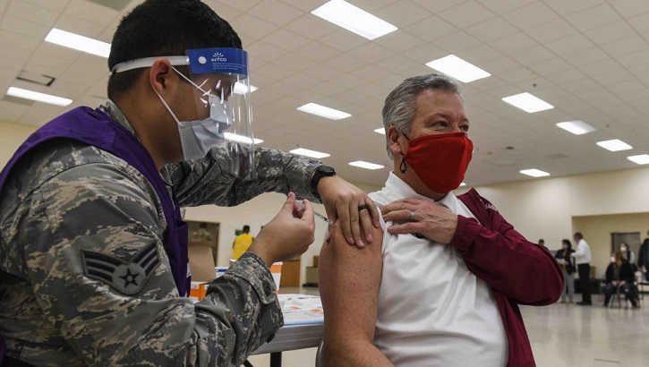 Image of Military health personnel wearing a mask giving the COVID-19 vaccine to a man who is also wearing a face mask. Click to open a larger version of the image.
