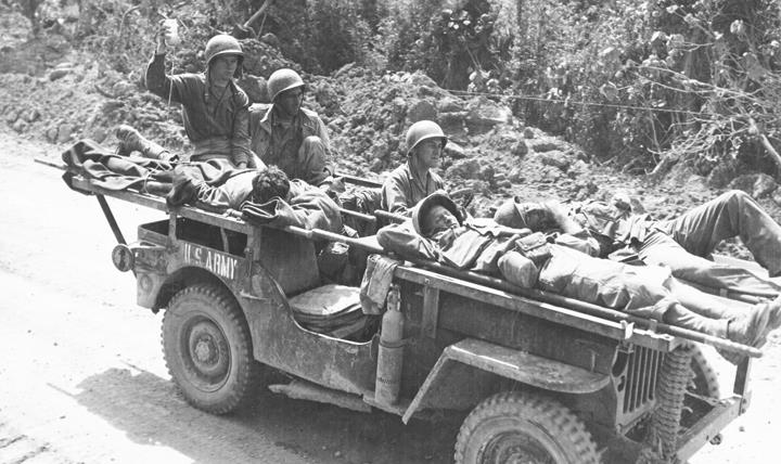 As an ambulance jeep evacuates three wounded U.S. soldiers to a rear area field hospital, one is given blood plasma en route by corpsmen of 102nd Medical Battalion. On Okinawa, April 22, 1945. (Otis Historical Archives, National Museum of Health and Medicine)