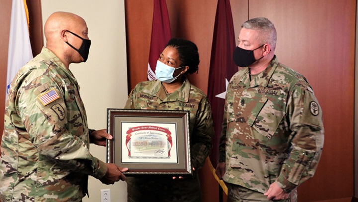 Image of Three military personnel, wearing masks, standing on a stage and holding an award.