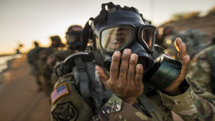 Image of Military personnel putting on a gas mask. Click to open a larger version of the image.