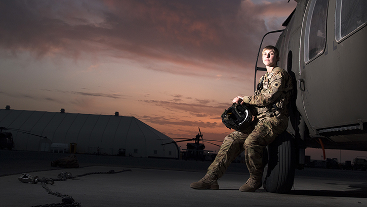 Female soldier, leaning against a military vehicle, at sunset